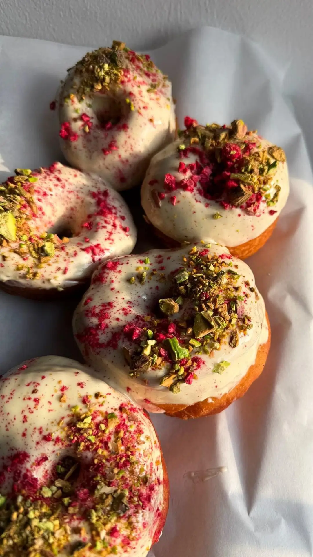 Friss, kézműves fánkok pisztáciás és málnás feltéttel a cukrászda desszertkínálatából.