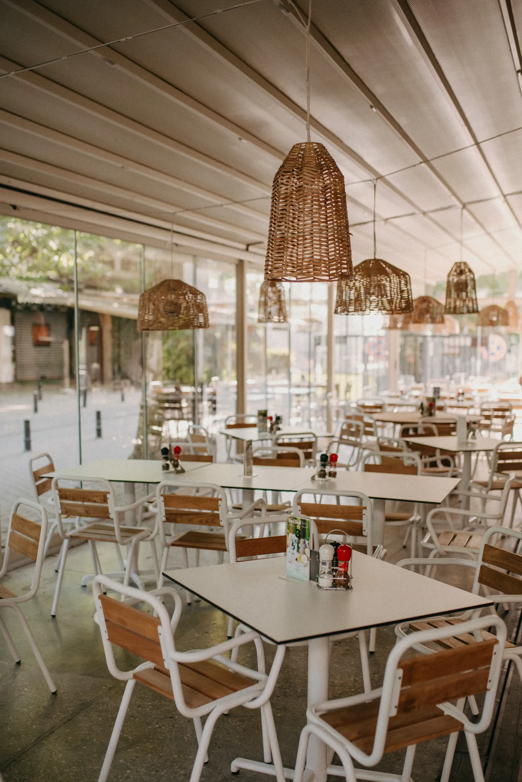 Hangulatos, fedett éttermi terasz berendezése fonott lámpákkal – ideális bérelhető helyszín nyári eseményekhez.